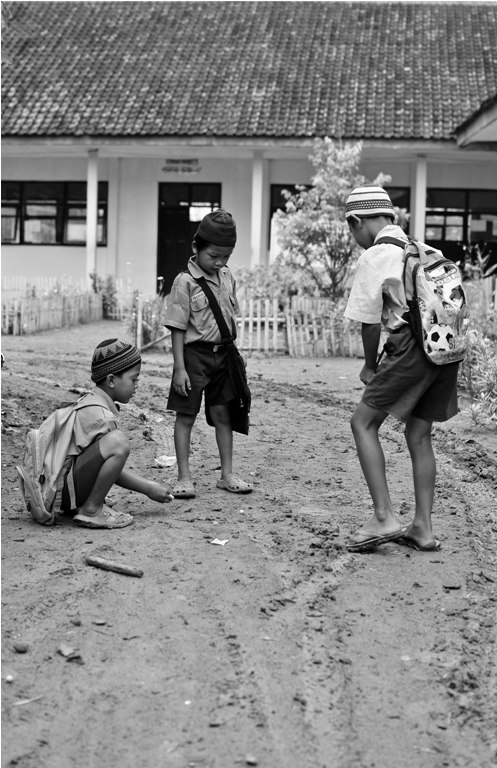 Anak-anak bermain kelereng di tanah yang becek